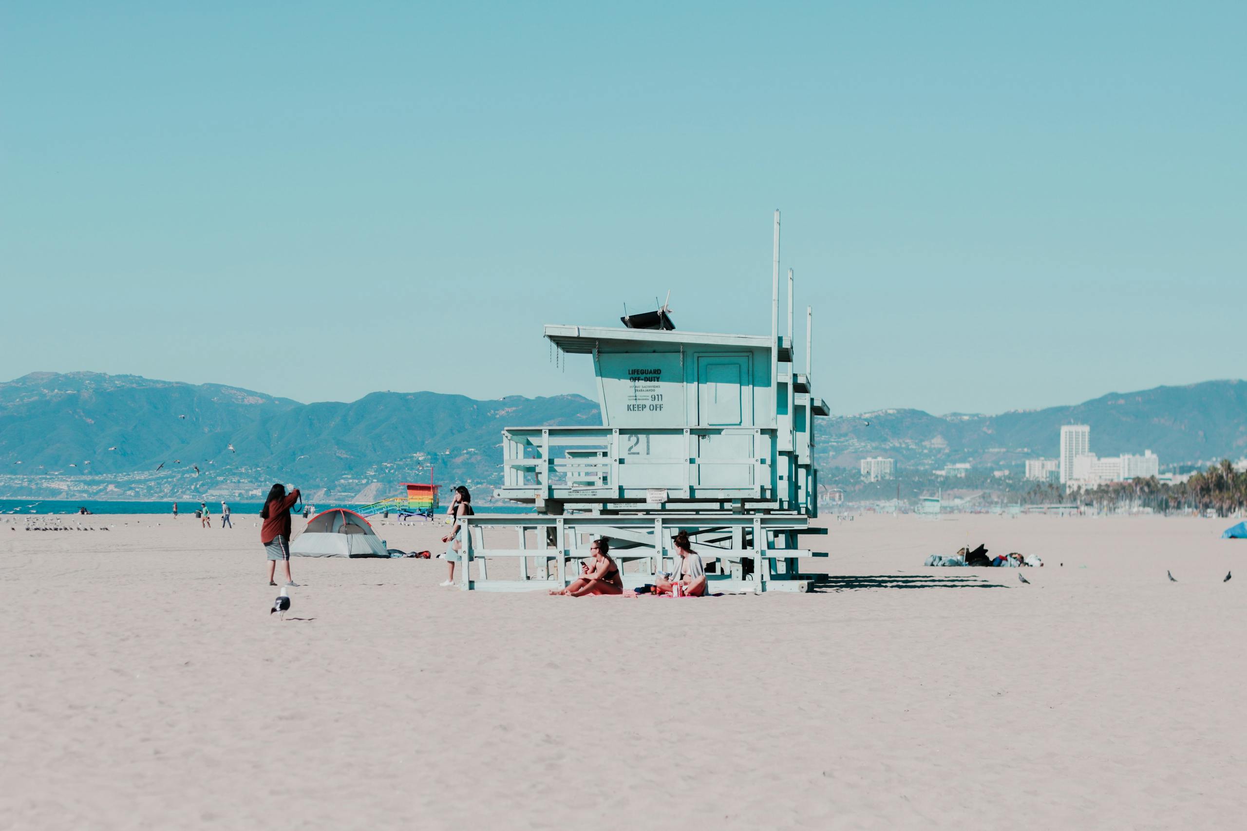 People Sitting on Sand Near White Wooden Cottage Near Seashore